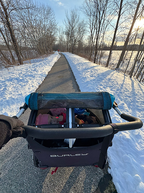 Kinderanhänger auf einem verschneiten Weg, gesehen aus der Perspektive des Schiebens